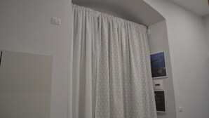 A room with a white door, a white curtain with a hexagonal pattern, and a wall-mounted picture. - Bassetto 013 (Naples)