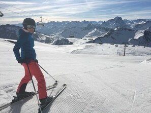 A person skiing on a snowy slope with a mountain range in the background and a ski lift in the distance.