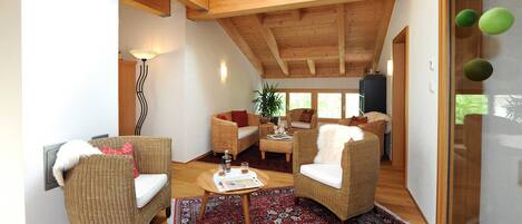 A spacious living area with wooden beams, wicker furniture, and a large window.