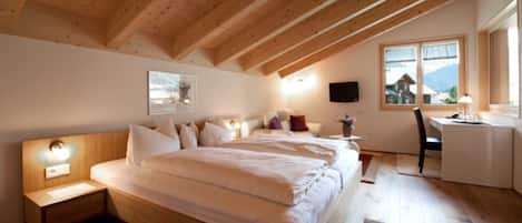 Une chambre avec un plafond en bois, un lit avec une literie blanche, une table de chevet avec une lampe, un bureau avec une chaise et une fenêtre donnant sur une montagne.