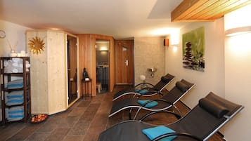 A spa room with wooden walls, a sun decoration, a towel rack, and a waiting area with chairs.