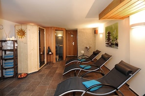Un cuarto de spa con paredes de madera, un adorno de sol, un perchero y una zona de espera con sillas.