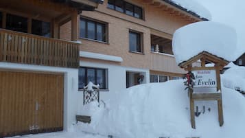 A wooden chalet with a sign reading 'Wohlfahrt Haus Evelin,' surrounded by snow.