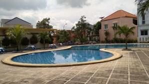 A swimming pool with a tiled deck, surrounded by palm trees and a few buildings in the background.