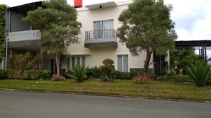 A modern building with a balcony, surrounded by various plants and a well-maintained lawn.