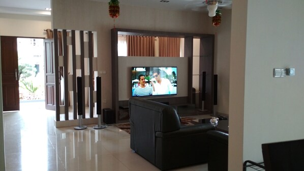 Una sala de estar moderna con televisor de pantalla plana, sofá de cuero negro y un panel decorativo en la pared.
