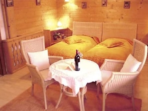 A room with a bed, two chairs, a small table, and a nightstand.