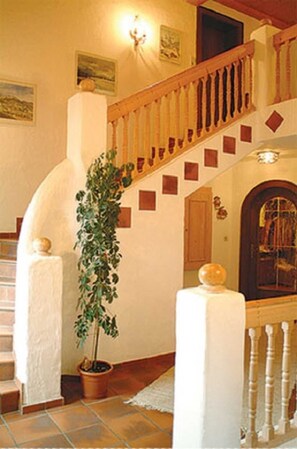 A staircase with a wooden handrail, a potted plant, and a wall with a light fixture and a door.