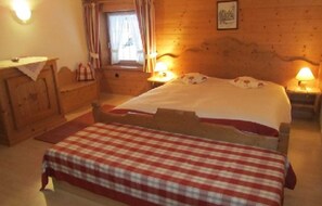 A wooden room with a bed, a nightstand, a dresser, and a window with curtains.