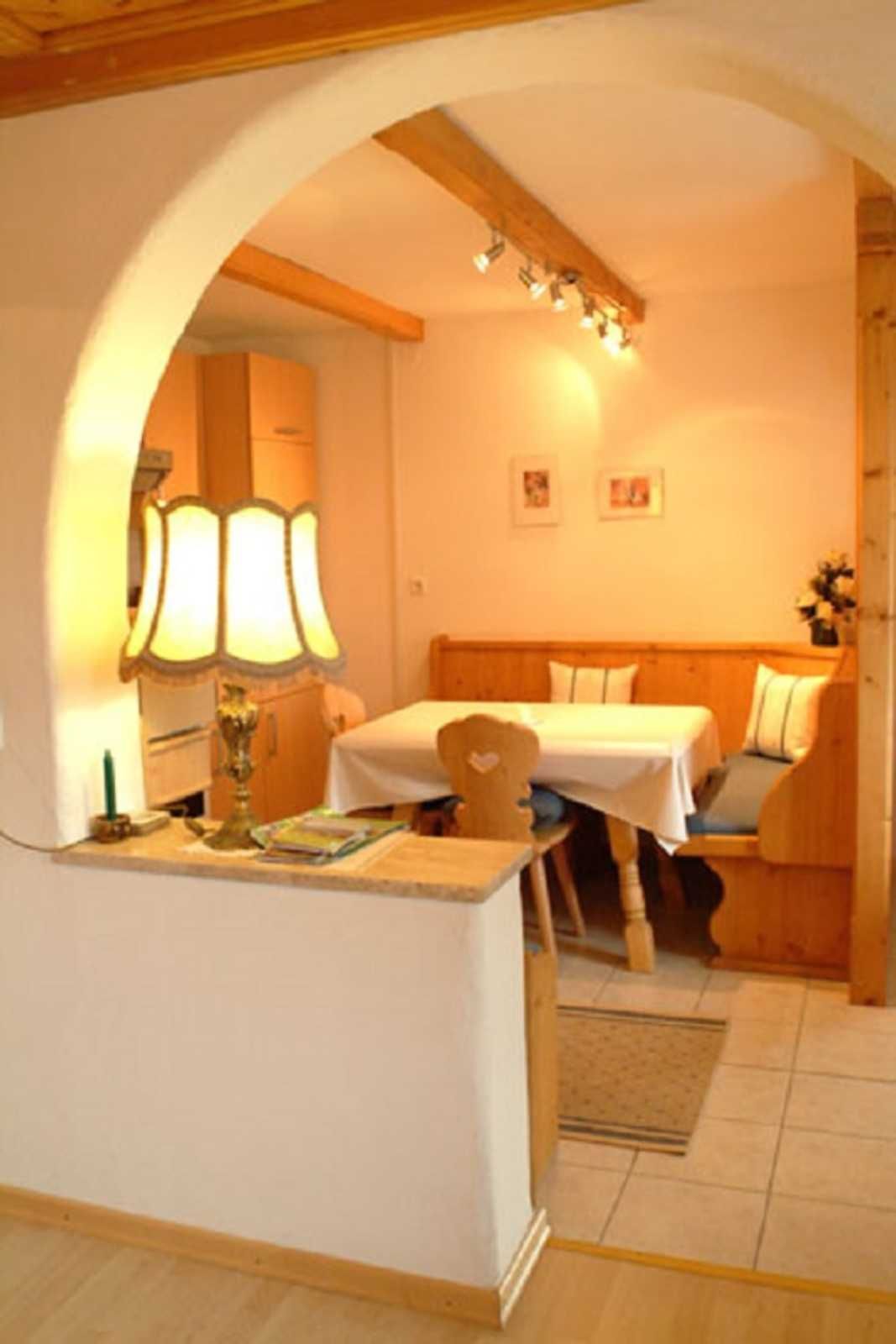 Une pièce chaleureuse avec un plafond en bois, un lit doté d’une tête de lit, une petite table avec une lampe et une étagère fixée au mur.