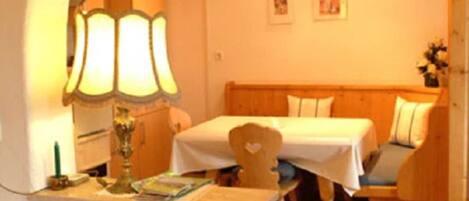 Une pièce chaleureuse avec un plafond en bois, un lit doté d’une tête de lit, une petite table avec une lampe et une étagère fixée au mur.
