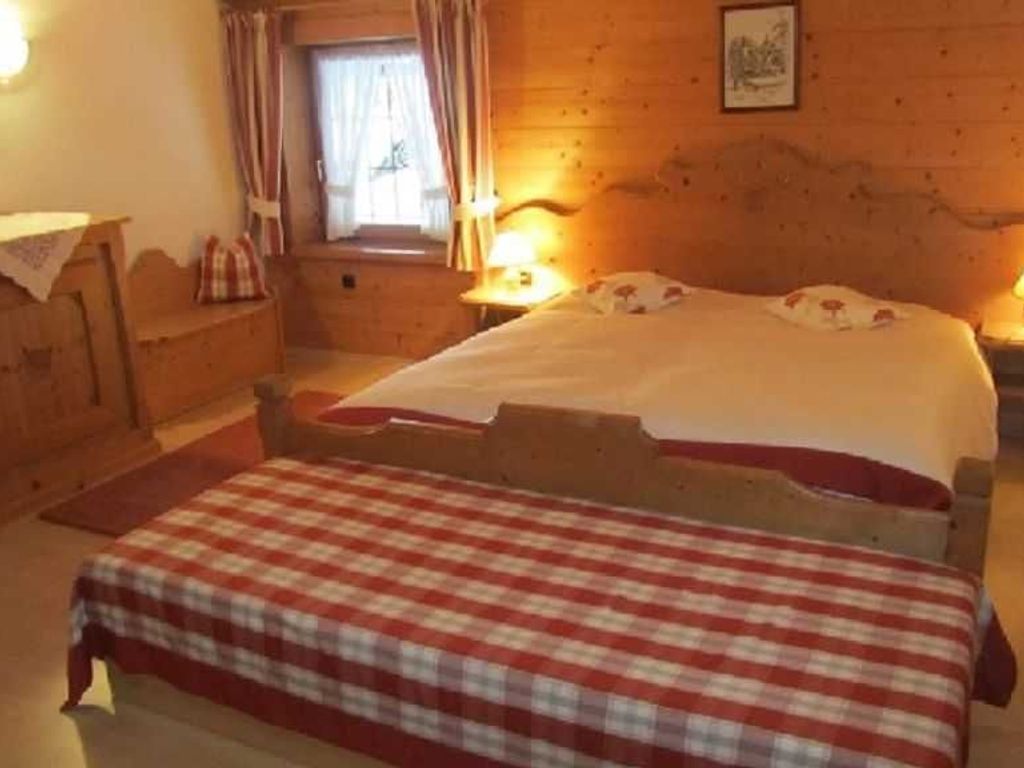 A wooden room with a bed, a nightstand, a window with curtains, and a wall-mounted picture.