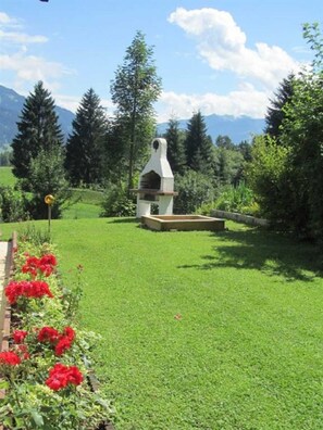A grassy area with a stone structure, possibly a fireplace, surrounded by trees and a mountain in the background.
