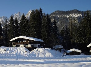 A lodge with a snow-covered roof, surrounded by snow and trees, with a mountain in the background.