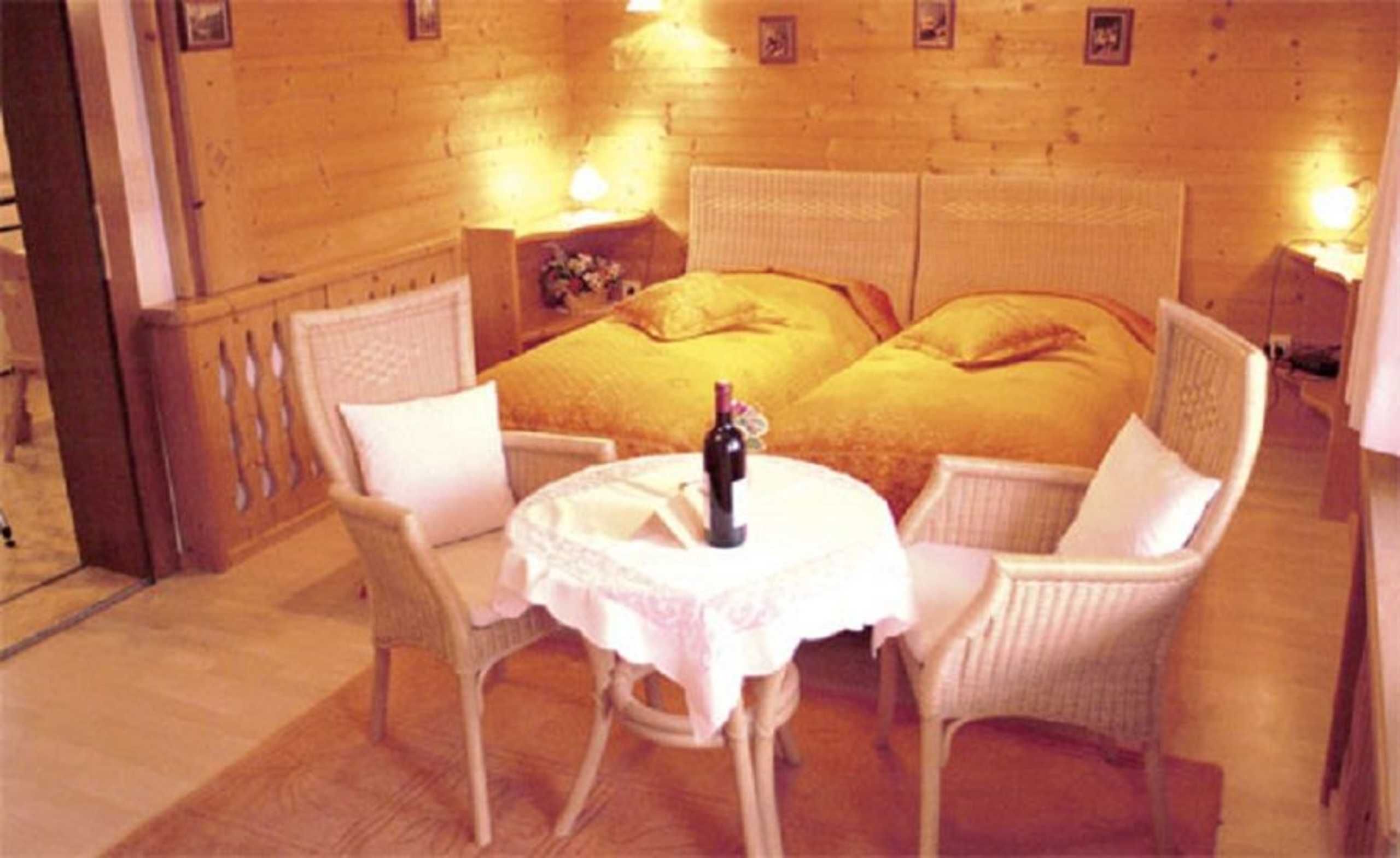 A cozy room with a bed, two chairs, a small table, and a bottle of wine.