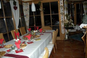 Un comedor con una mesa lista para comer, sillas alrededor y un árbol de Navidad al fondo.