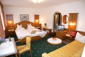 Habitación de hotel con cama, escritorio, silla, una pequeña mesa con frutero, televisor y espejo.