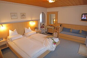 A hotel room with a large bed, a desk, a sofa, a TV, and a mirror. - Vacation apartment Landleben for 4-5 persons - Landhaus Dengg (Gerlos)