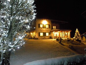 A building with a sign 'Landhaus Denga' at night, surrounded by snow and Christmas lights.