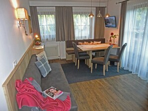 A cozy living area with a sofa, dining table, and chairs, a radiator, and a TV on the wall. - Vacation apartment Landleben for 4-5 persons - Landhaus Dengg (Gerlos)