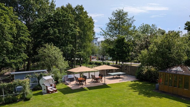 Ein gepflegter Außenbereich mit Terrasse, Tisch und Stühlen, umgeben von üppigem Grün und Bäumen.
