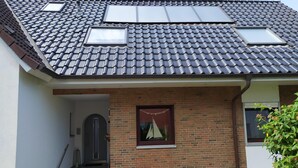 Ein zweistöckiges Haus mit einem Ziegeldach, einer Ziegel-Fassade und einer kleinen Veranda mit einer Bank.