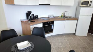 Eine kompakte Küche mit Mikrowelle, Kaffeemaschine, Toaster, Spüle und Backofen. Ein Esstisch mit Stühlen und Untertasse ist ebenfalls vorhanden.