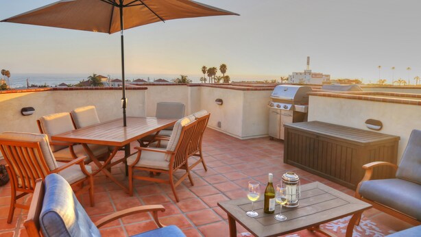 Eine Terrasse mit Holztisch, Stühlen, einem Grill und Blick auf das Meer.
