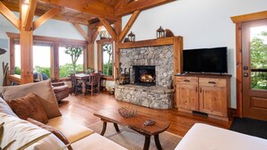 A cozy living room with a stone fireplace, wooden beams, a television, and comfortable seating.