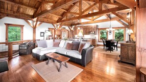 A spacious living area with a wooden ceiling, a sectional sofa, a dining table, and a kitchen in the background.