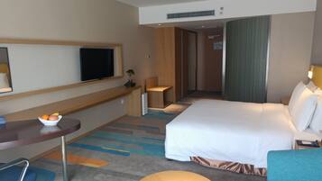 A hotel room with a bed, a desk with a chair, a television, and a small table with a bowl of fruit.