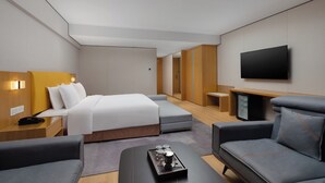 A modern hotel room with a bed, sofa, TV, and a small table with a tray.