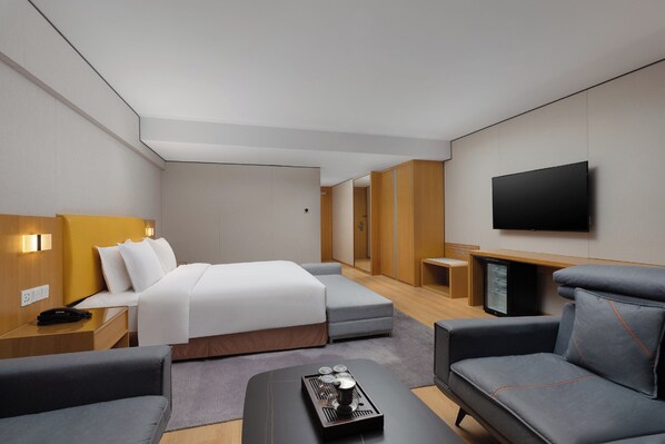 Une chambre d’hôtel moderne équipée d’un lit, d’un canapé, d’une télévision et d’une petite table avec un plateau.