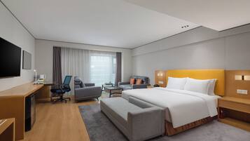 A hotel room with a bed, a desk, a chair, a sofa, a TV, and a window with curtains.