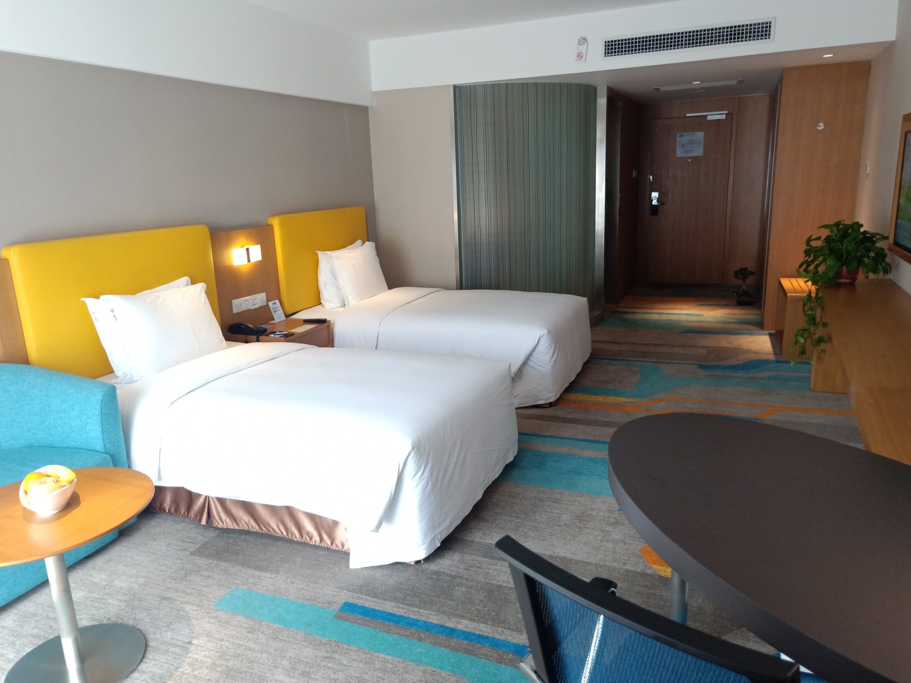 A hotel room with two beds, a small table, a chair, and a desk.