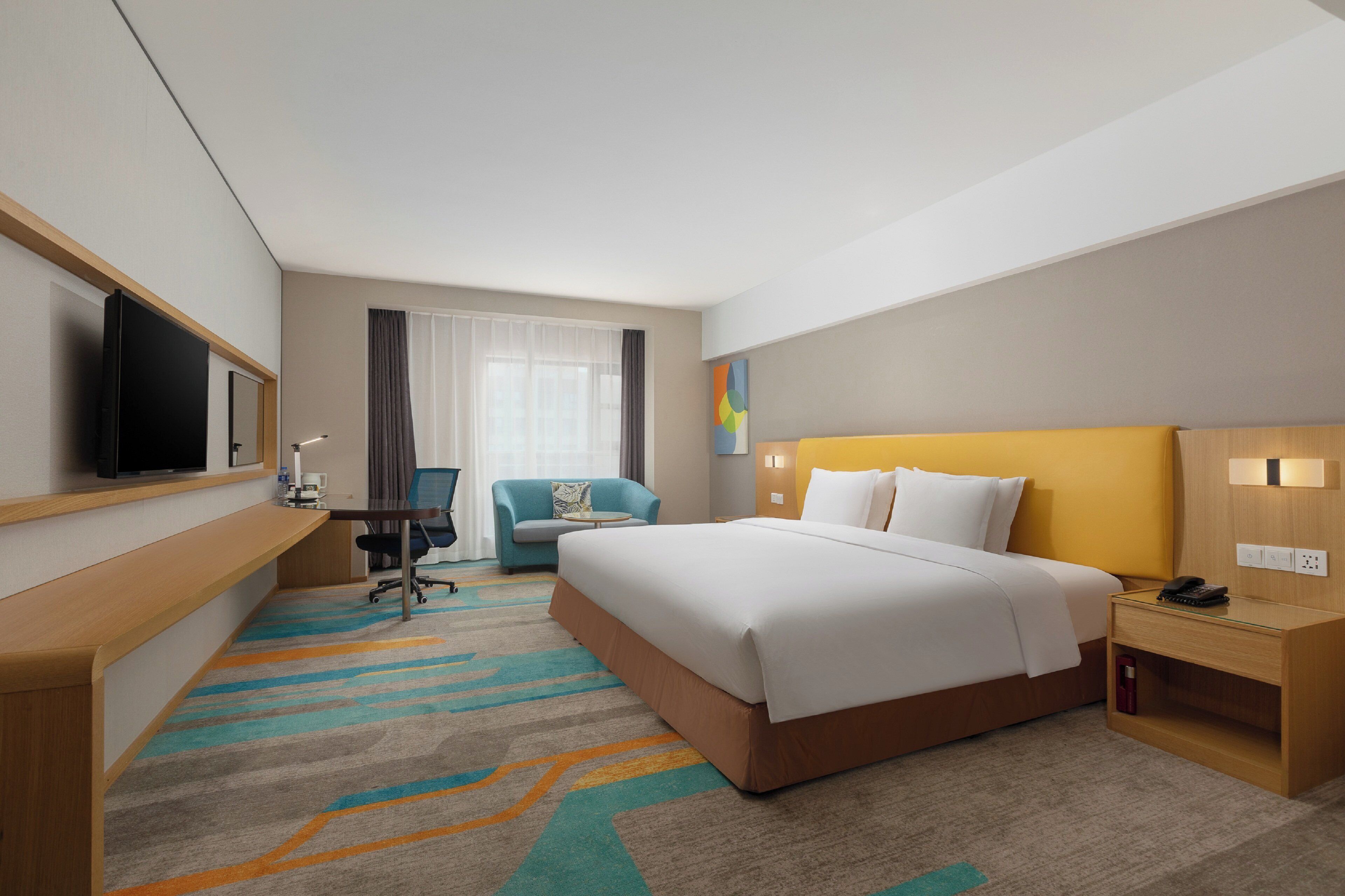 A hotel room with a bed, a desk, a chair, a television, and a window with curtains.