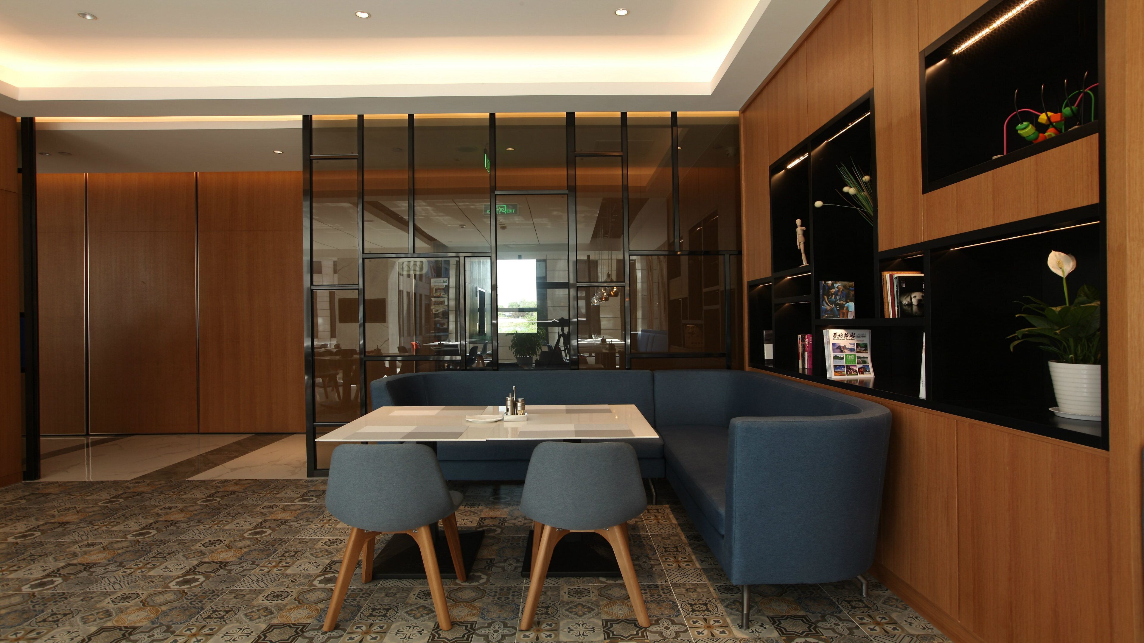 A modern interior with a dining area featuring a table and chairs, a sofa, and a wall with a display shelf.