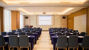 A conference room with rows of tables and chairs, a projector screen, and a presentation screen.