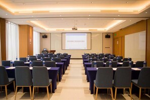 Une salle de conférence avec des rangées de tables et de chaises, un écran de projection et un écran de présentation.