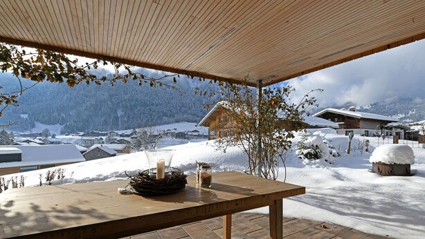 A wooden table with candles and a glass jar, set outdoors with a view of snow-covered houses and mountains. - MAC's Apartment - MAC's Apartment (Au)