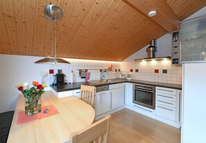 A modern kitchen with wooden ceiling, white cabinets, stainless steel appliances, and a dining area with a vase of flowers.
