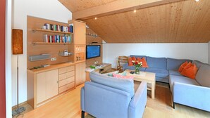 A modern living room with a loft-style ceiling, built-in shelving, a flat-screen TV, a sofa, and a coffee table. - MAC's Apartment - MAC's Apartment (Au)