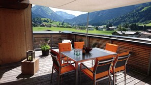 A wooden deck with a table and chairs, a potted plant, and a bottle of wine.