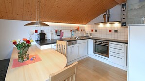 A modern kitchen with wooden ceiling, white cabinets, stainless steel appliances, and a dining area with a vase of flowers. - MAC's Apartment - MAC's Apartment (Au)