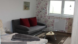 Une petite chambre à coucher moderne, avec un lit, un canapé, une table basse en verre et un radiateur.