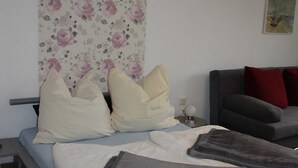 Une chambre à coucher avec un lit, des oreillers, un canapé gris et un papier peint à motifs floraux.