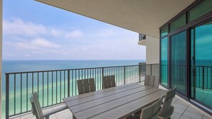 Uma varanda com mesa e cadeiras, com vista para um mar turquesa e céu claro.