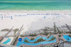 Luchtbeeld van een strandresort met een groot zwembad, strandparasols en een wachthuisje.