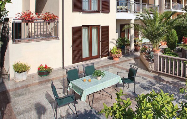 An outdoor patio with a table and chairs, surrounded by potted plants and a balcony with flowers.