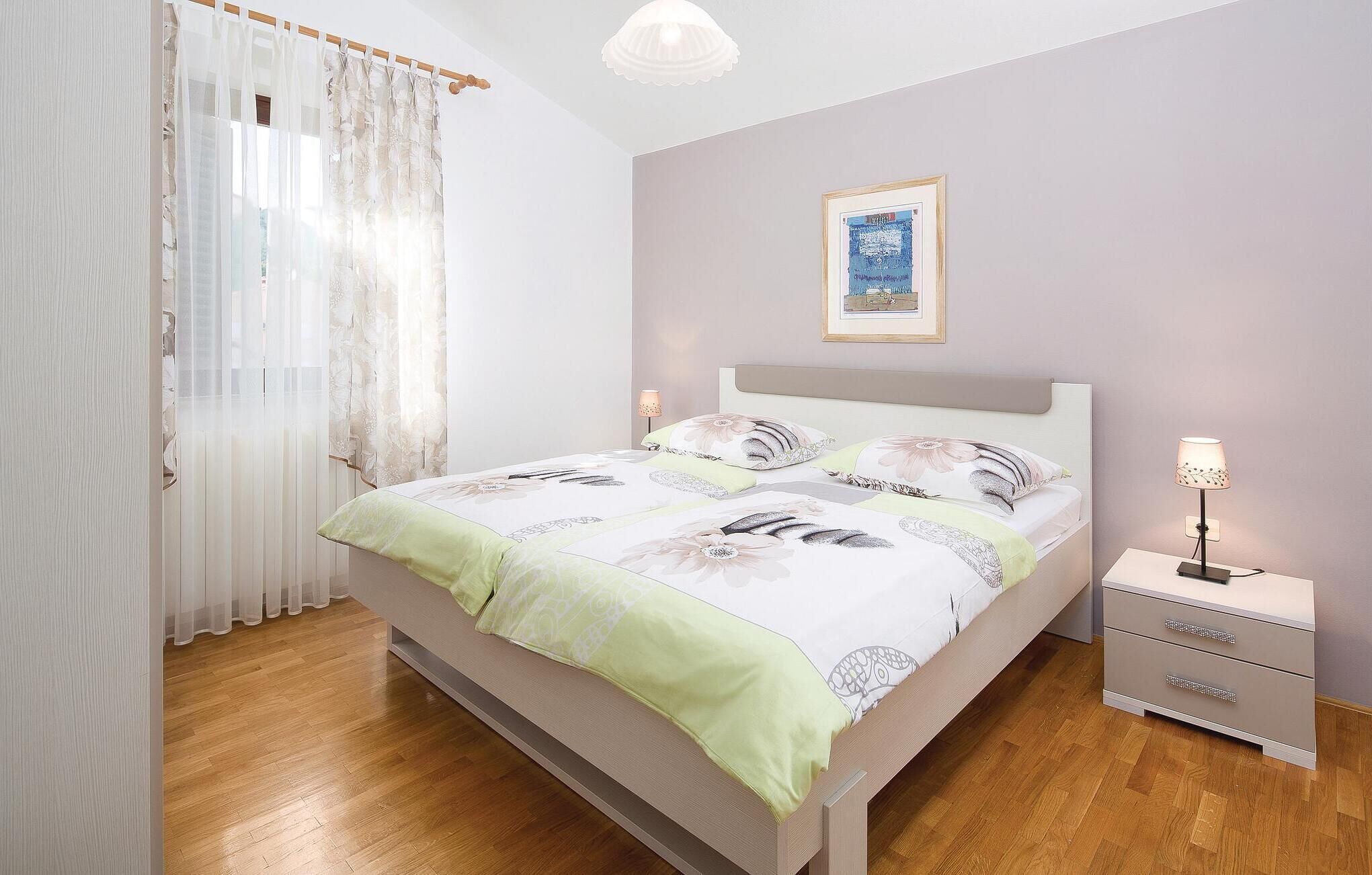 Un dormitorio con cama, mesitas de noche, una lámpara y un cuadro en la pared.